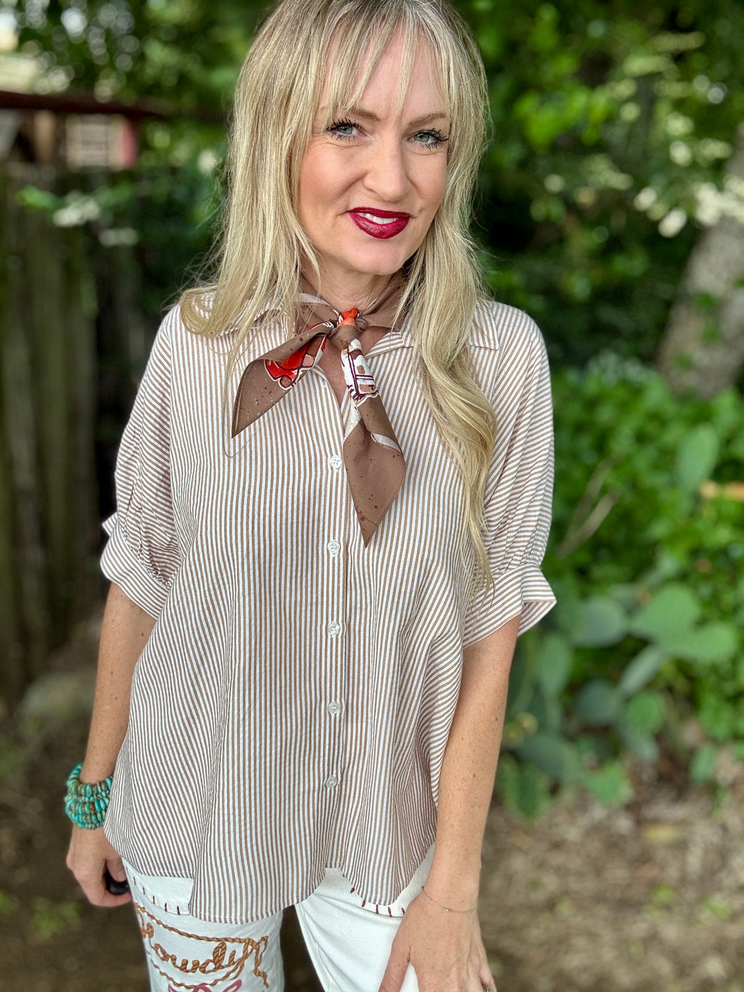 Woman wearing a striped shirt with a brown scarf around her neck, standing outdoors.