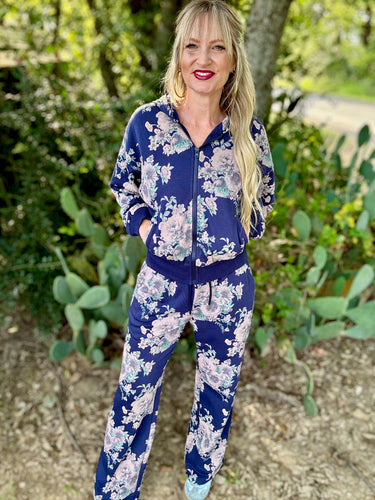 Woman wearing a blue floral tracksuit standing outdoors with greenery in the background