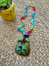 Colorful beaded necklace with a green pendant on a woven surface