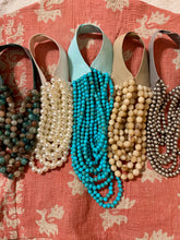 Set of necklaces with different bead colors hanging on a pink floral fabric background